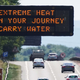 A sign above a highway filled with cars shows a warning message about the extreme heat.